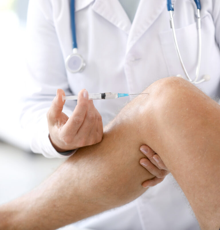 Close-up of a doctor administering an injection into a male athlete’s knee inside a clinical setting, focusing on the medical procedure.