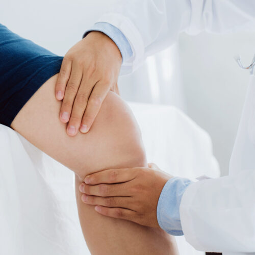 Doctor and physiotherapist examining and treating a patient’s injured knee, discussing options such as platelet-rich plasma (PRP) therapy.
