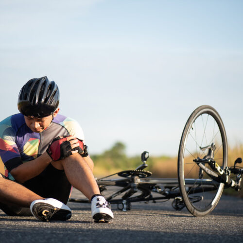 Man cyclist with injured knee after falling off his bike, sitting on the ground beside his bicycle after a cycling accident.