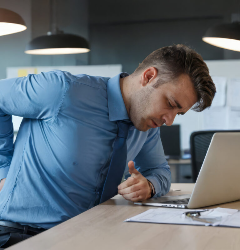 Office worker experiencing lower back pain while seated at a desk, highlighting musculoskeletal pain from poor posture, prolonged sitting, or lack of ergonomic support.