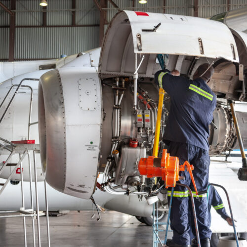 Two mechanics working on heavy machinery on an airplane, highlighting the risks of airport jobs, including injury from equipment or repetitive physical tasks.