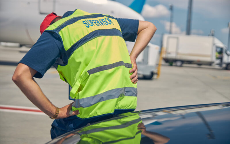 Airport male worker doubled over in acute pain while on duty, indicating a sudden injury or medical emergency at the workplace.