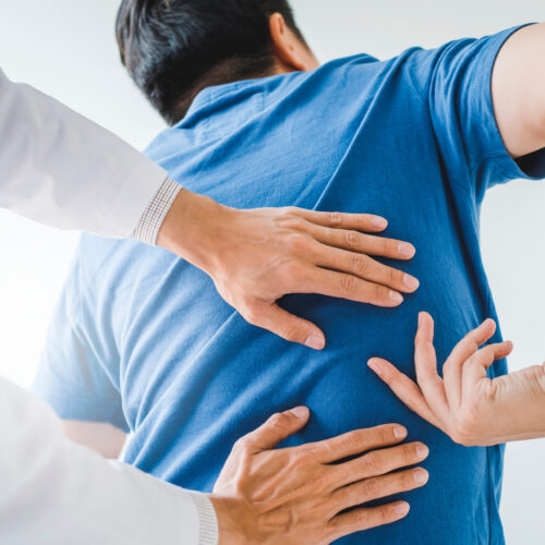 A medical professional in a clinical setting examines a patient's back, pointing out areas of concern during a physical therapy consultation.