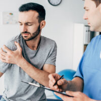 Patient showing shoulder pain from injury to a physiatrist during consultation.