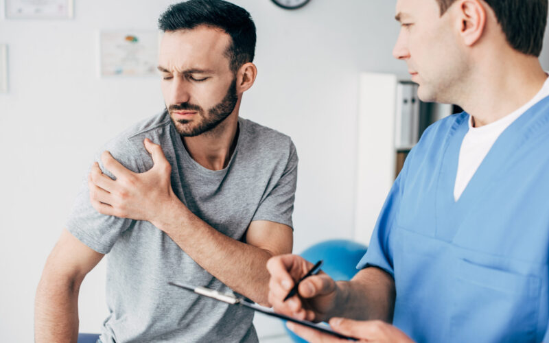 Patient showing shoulder pain from injury to a physiatrist during consultation.