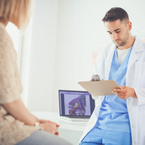 Male physician assistant in blue scrubs standing in a medical office, attentively providing injury care to a patient.