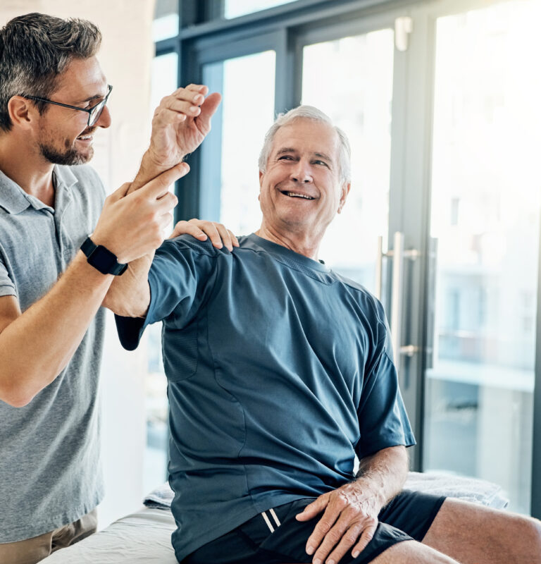 With a smile, a senior man performs arm-exercises under the guidance of a physical therapist in a rehabilitation clinic, focusing on improving strength and mobility.