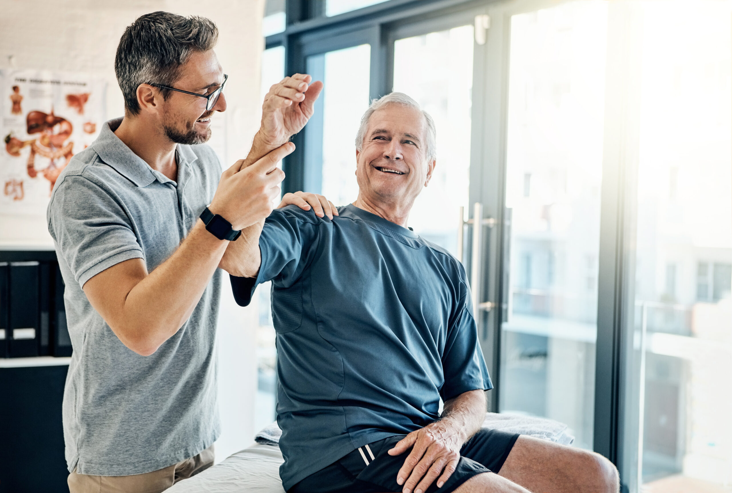 With a smile, a senior man performs arm-exercises under the guidance of a physical therapist in a rehabilitation clinic, focusing on improving strength and mobility.