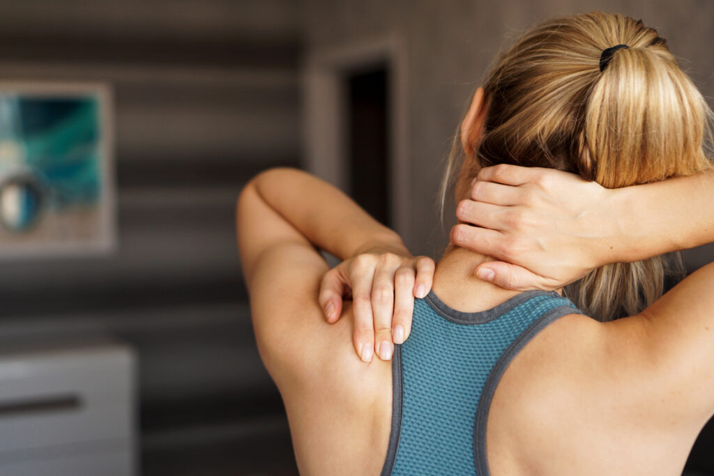 Young woman holding her neck in pain showing delayed neck pain or muscle strain from exercise.