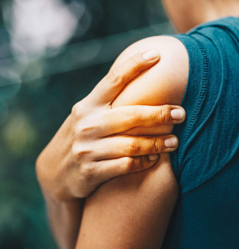 Man holding her shoulder in pain, illustrating muscle or nerve-related shoulder discomfort.