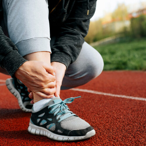 Runner clutching her ankle on the track due to pain from a reinjury caused by a misstep.