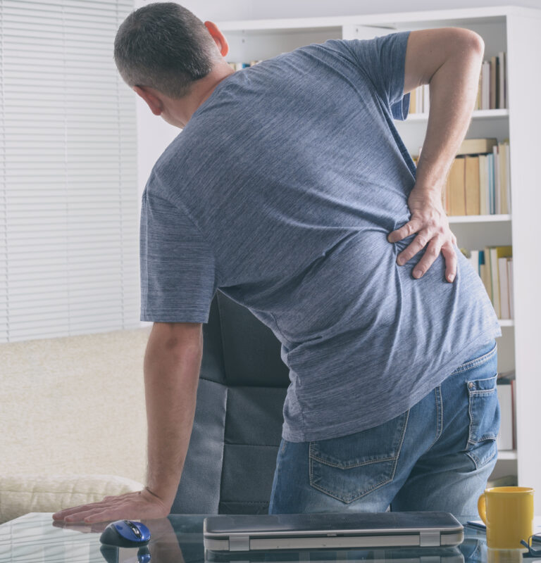 Man holding his lower back while experiencing pain from a possible reinjury.