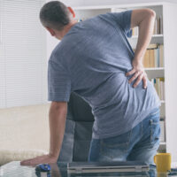 Man holding his lower back while experiencing pain from a possible reinjury.