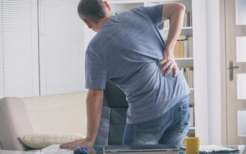 Man holding his lower back while experiencing pain from a possible reinjury.
