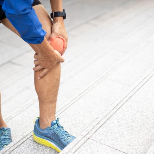Man standing outdoors holding his knee, showing referred knee pain.