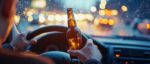 Intoxicated driver holding a beer bottle while behind the wheel in traffic, illustrating the danger of impaired driving accidents.