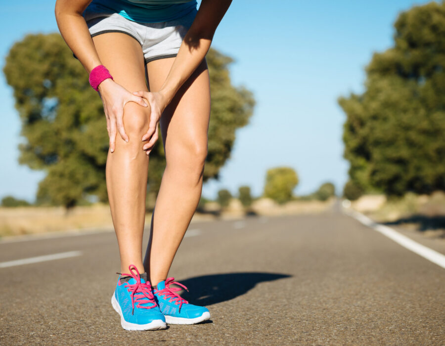 Woman running outdoors while holding her knee, illustrating knee pain during physical activity.