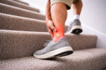 Person walking up carpeted stairs while holding their ankle, illustrating ankle pain or ankle cracking during movement.
