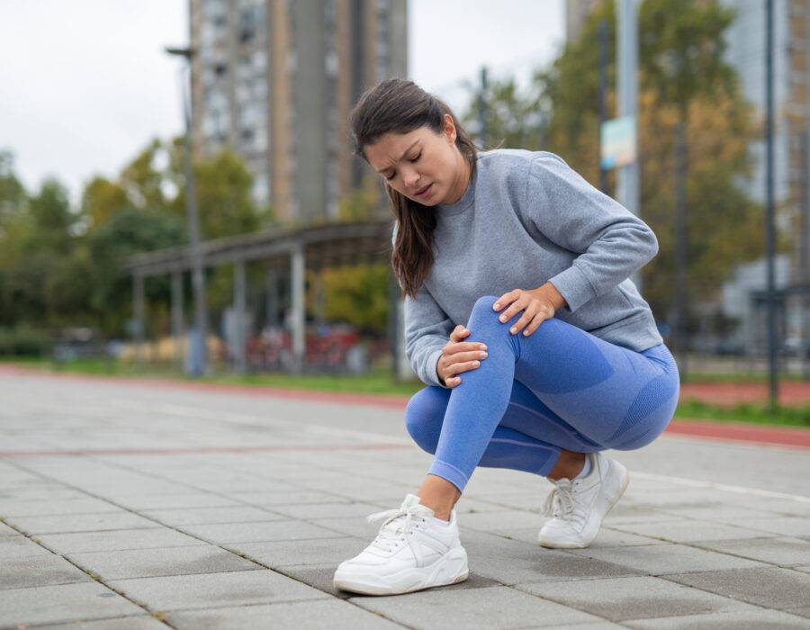 Woman experiencing sharp knee pain during outdoor exercise, showing sharp pain in the body during movement.