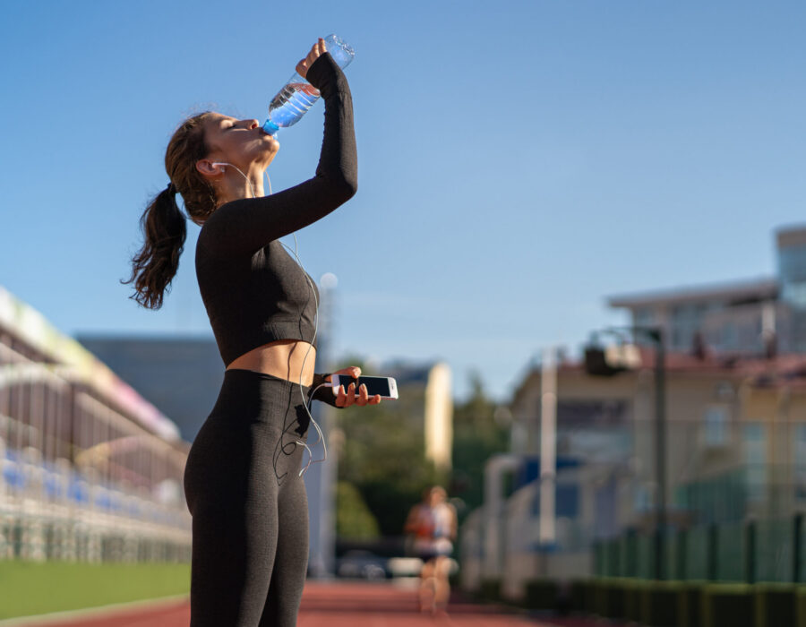 young woman drinking water after running on a track, representing healthy lifestyle and daily wellness habits.