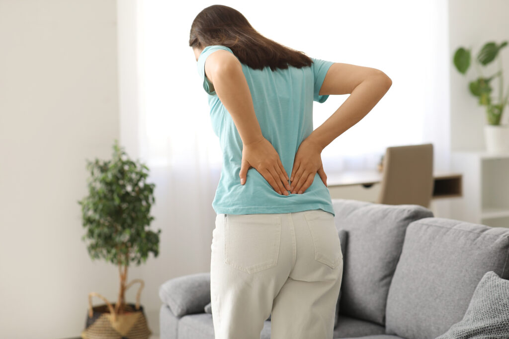 Woman holding her lower back while dealing with recurring pain during everyday activities at home.
