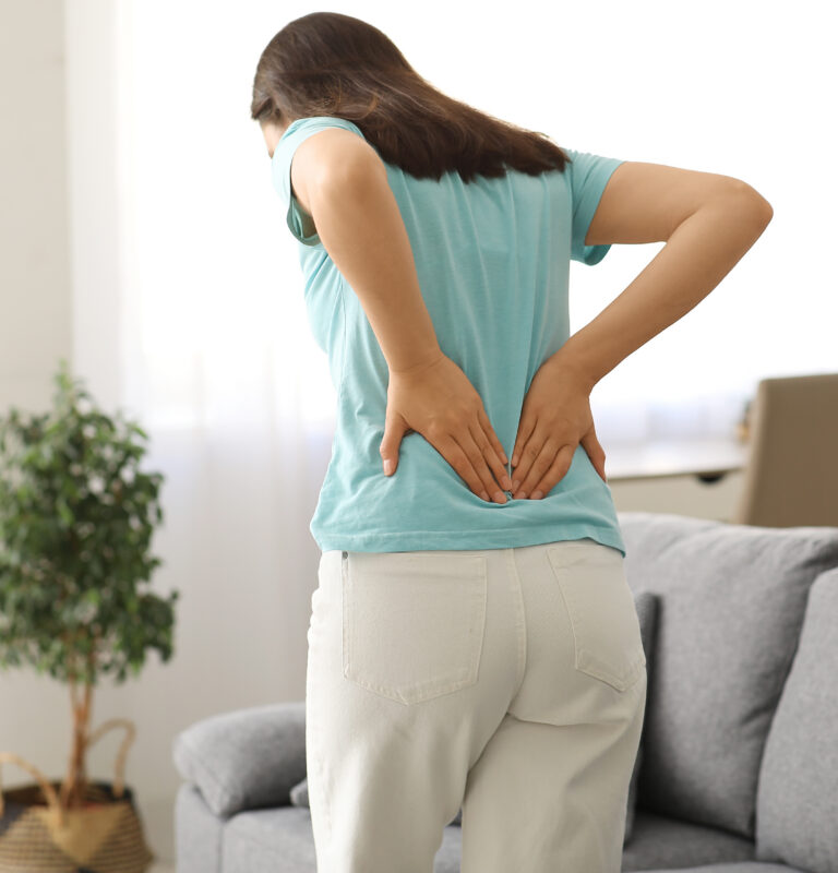 Woman holding her lower back while dealing with recurring pain during everyday activities at home.