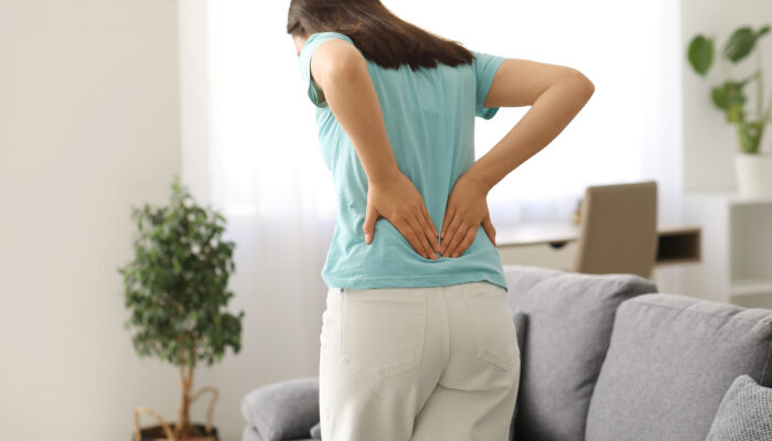 Woman holding her lower back while dealing with recurring pain during everyday activities at home.
