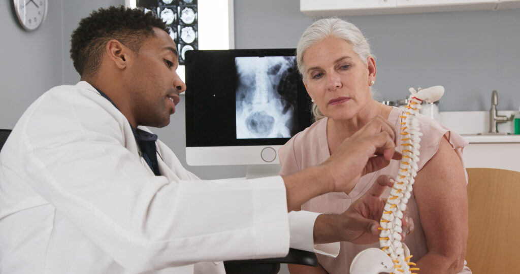 Physician explaining spinal anatomy and nerve pathways to a patient experiencing pinched nerve symptoms.