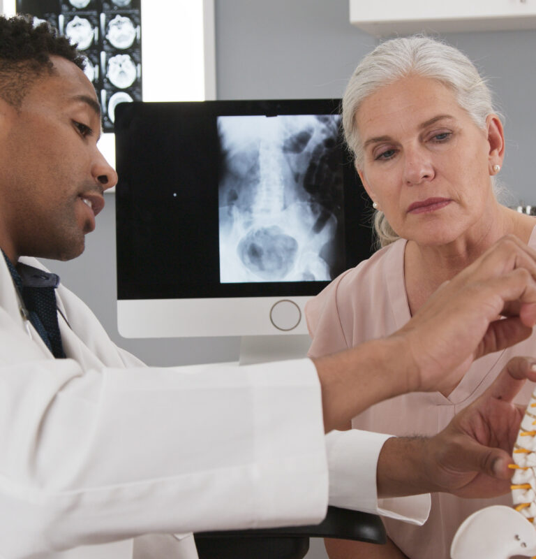 Physician explaining spinal anatomy and nerve pathways to a patient experiencing pinched nerve symptoms.