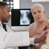 Physician explaining spinal anatomy and nerve pathways to a patient experiencing pinched nerve symptoms.