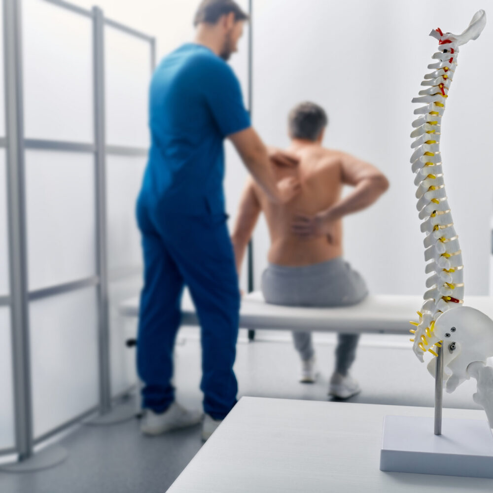 Diagnosing a Bulging Disc or Herniated Disc Healthcare provider evaluating a patient for a bulging or herniated disc with a spine model in the foreground.