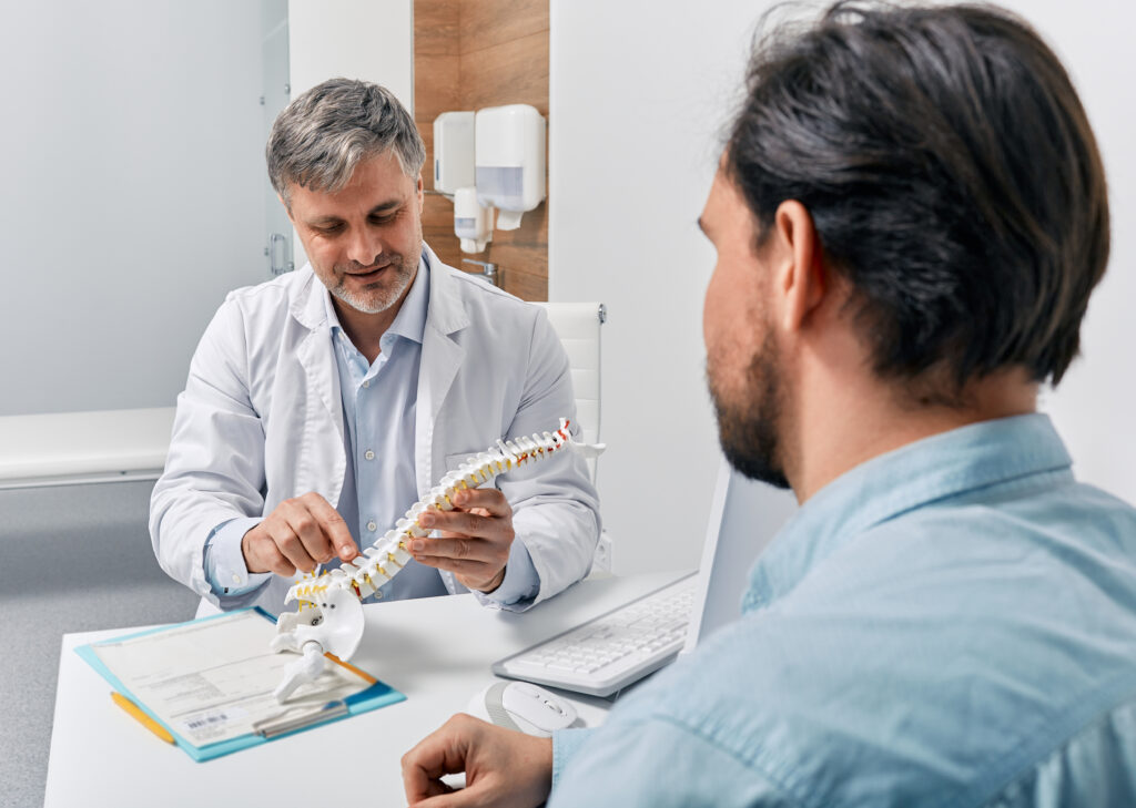 Discussing Treatment Options for a Bulging or Herniated Disc Physician explaining a spine model to a patient during a consultation about a bulging disc or herniated disc.