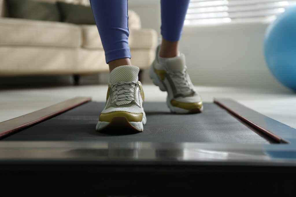 Close-up of supportive athletic shoes walking on an under-desk treadmill during a home workout.