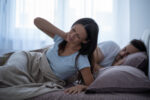 Woman waking up with neck pain after sleeping in bed and holding the side of her neck.