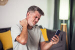 Man with neck pain looking at a smartphone while using ChatGPT for injury symptoms after an accident.