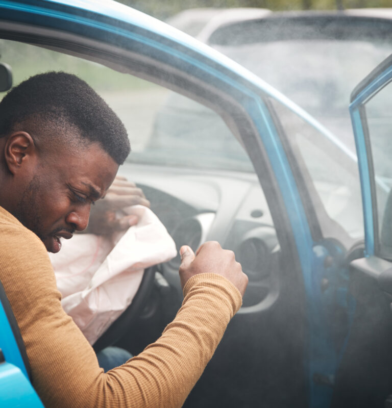 Driver experiencing pain after airbag deployment following a car accident, illustrating common airbag deployment injuries and post-crash symptoms.