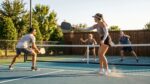 Group of friends playing doubles pickleball on an outdoor court on a sunny fall day